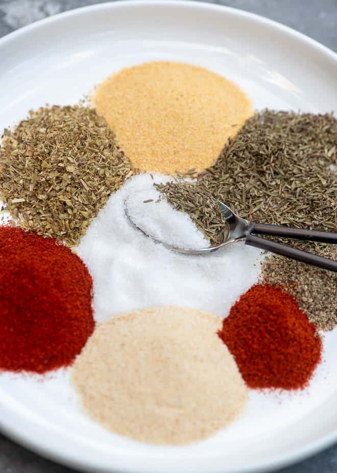 A closeup image of the spices on a white plate being scooped up with a small spoon.