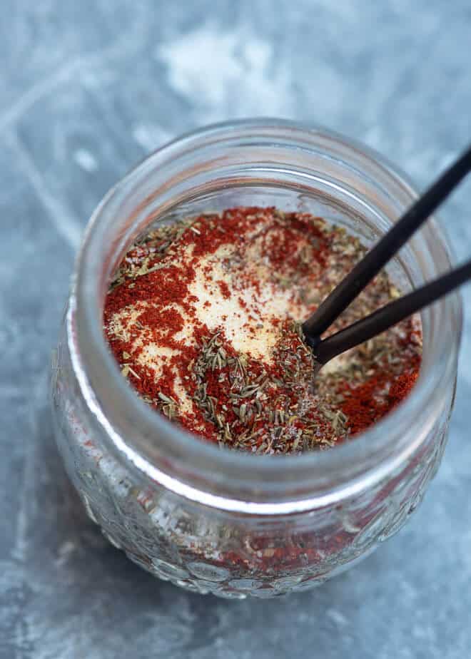  An over the top image of spices in a mason jar with a spoon on a grey board.