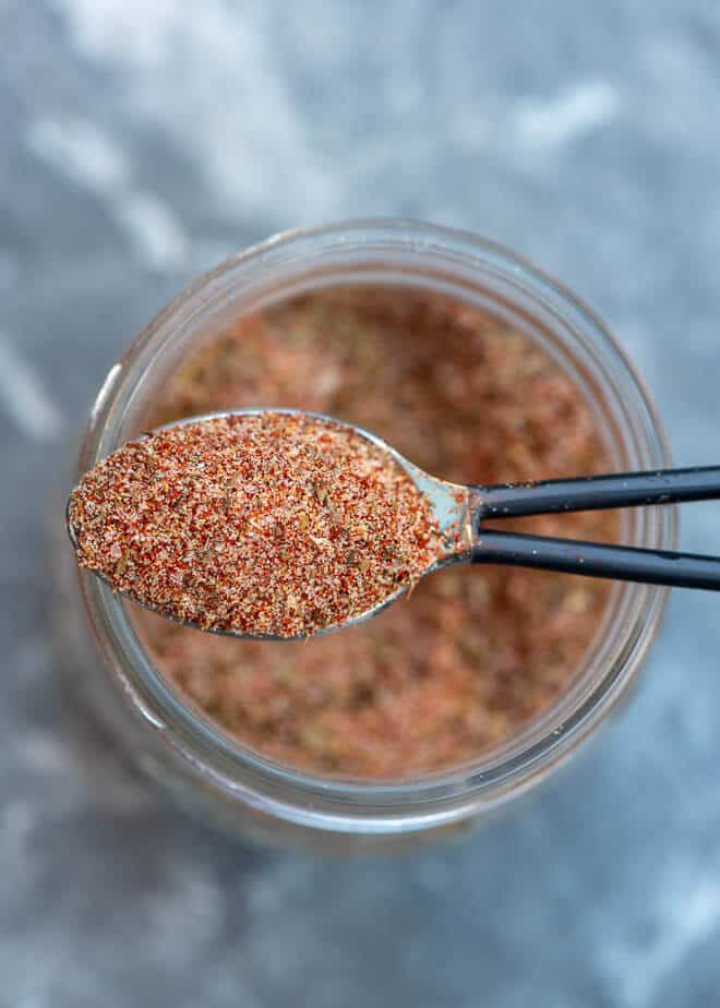 An overhead image of a small spoon lifting some of the  Kickin’ Cajun Seasoning Mix from a mason jar.