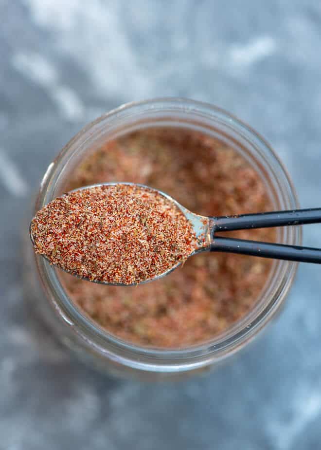 A spoon lifts seasoning from a jar.