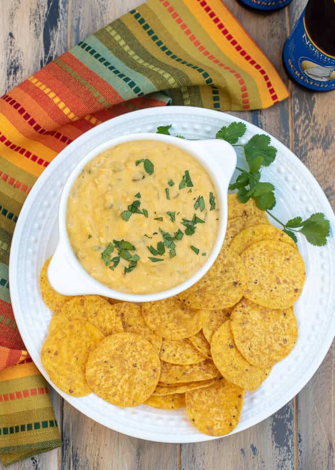 A small white bowl of dip on a white plate with tortilla chips.