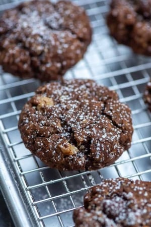 Chocolate cookies with nuts and powdered sugar on a wire rack.