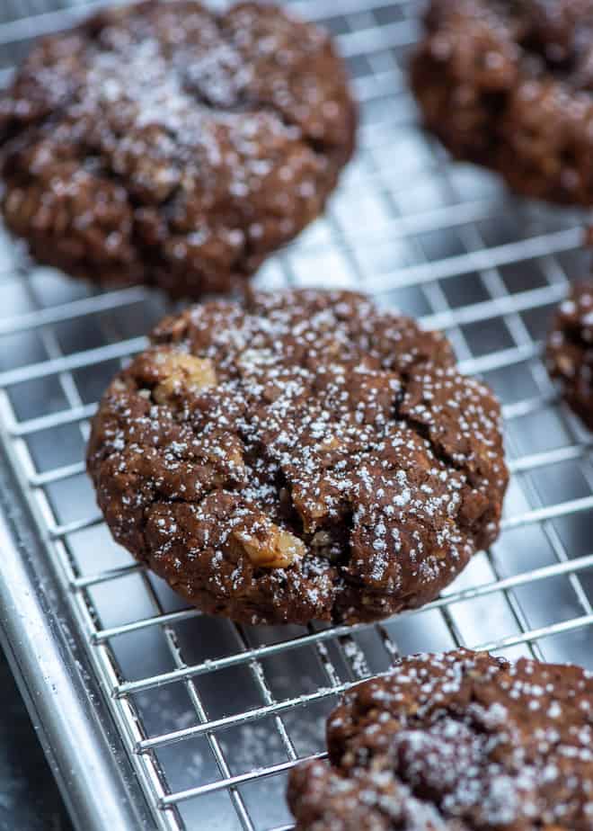Chocolate cookies with nuts and powdered sugar on a wire rack.