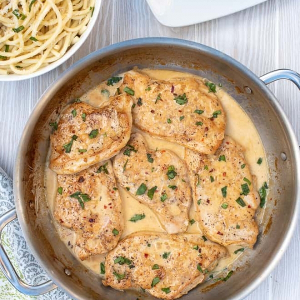 A skillet filled with a creamy sauce and slices of cooked chicken.