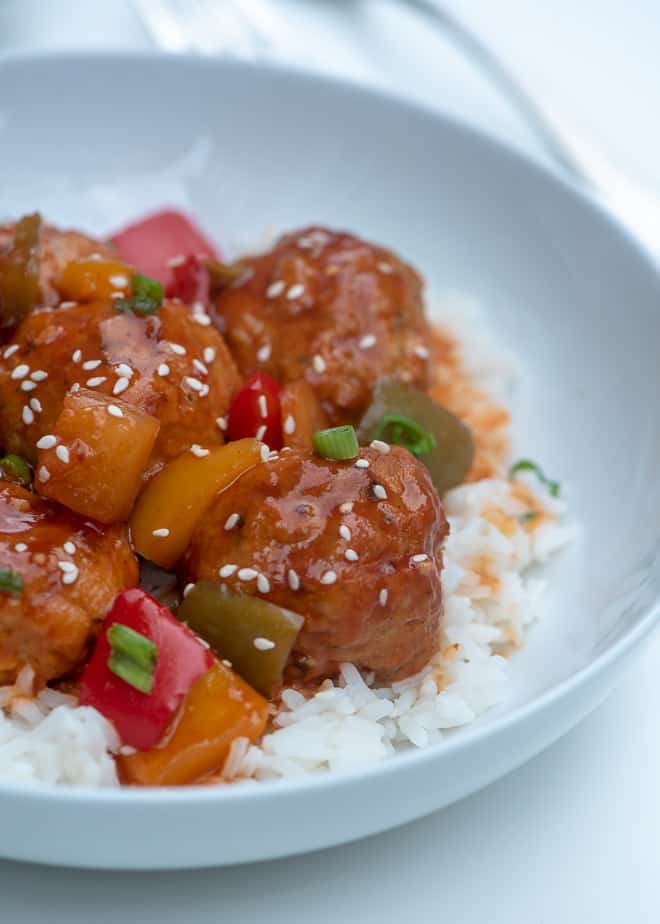 Slow Cooker Sweet and Sour Chicken Meatballs over rice in a white bowl.