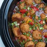 A slow cooker insert filled with chicken meatballs, sauce, and red bell peppers.