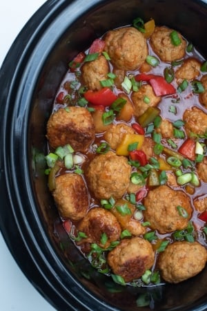 A slow cooker insert filled with chicken meatballs, sauce, and red bell peppers.