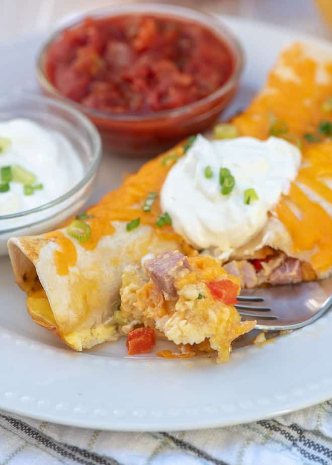 A breakfast enchilada with a fork on a white plate.