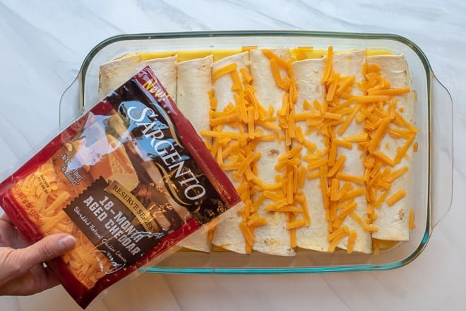 Pouring the Sargento Reserve Series Shreds over the enchiladas in the baking dish.
