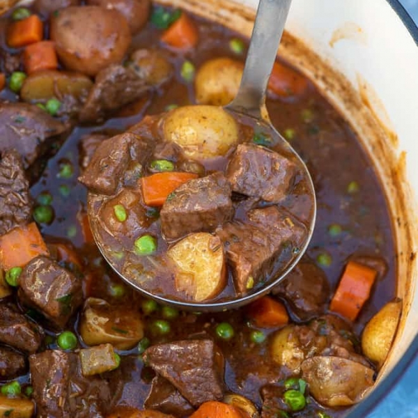 A ladle scoops up beef stew from a pot.