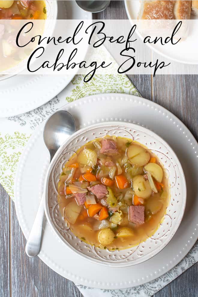 An over the top shot of Corned Beef and Cabbage Soup in a white bowl on a white plate with a spoon with overlay text.