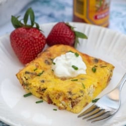 A piece quiche topped with sour cream with strawberries on a white plate.
