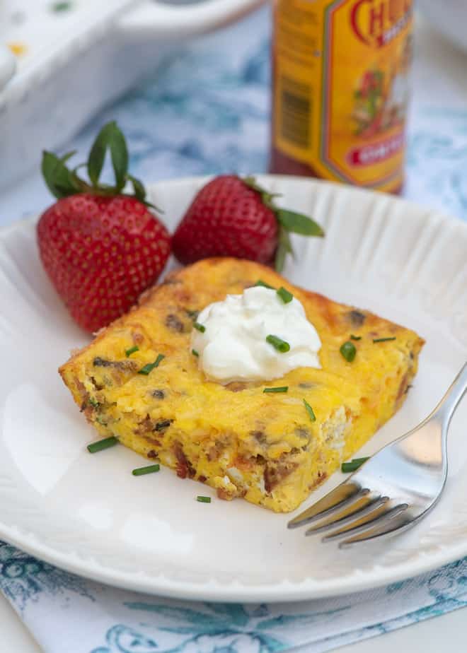 A slice of Easy Crustless Quiche topped with sour cream on a white plate with strawberries.