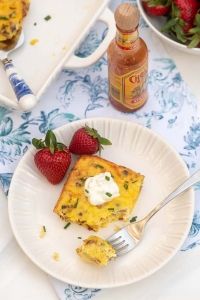 A slice of quiche topped with sour cream on a white plate with strawberries.