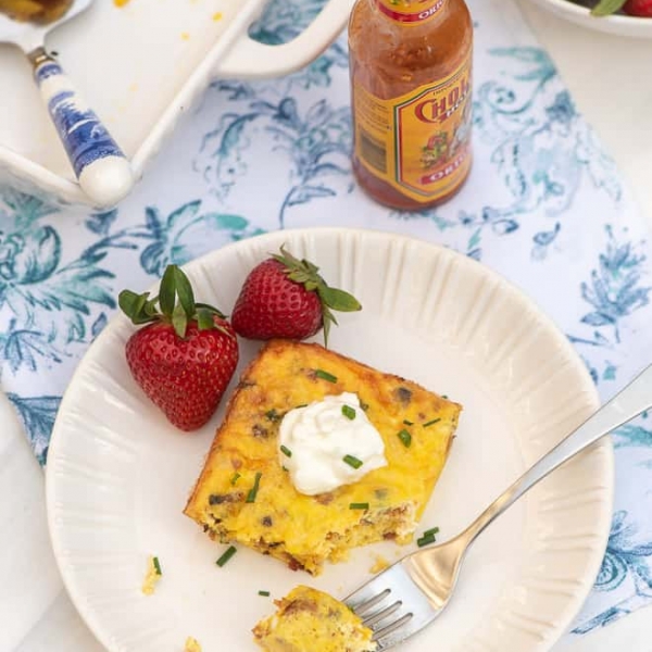 A slice of quiche topped with sour cream on a white plate with strawberries.
