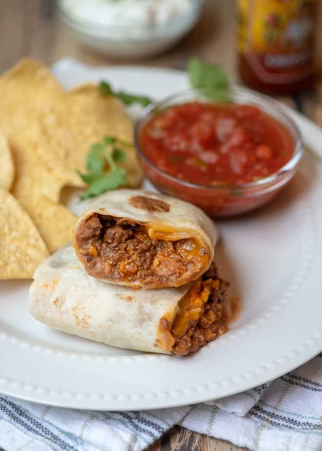 A burrito cut in half on a white place with tortilla chips and a small bowl of salsa.