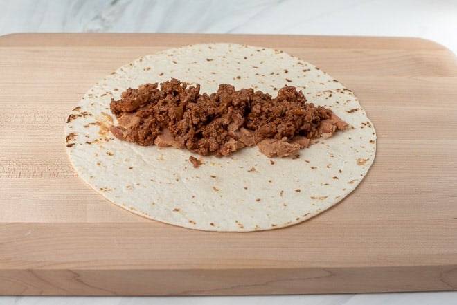 A flour tortilla with a layer of beans and beef