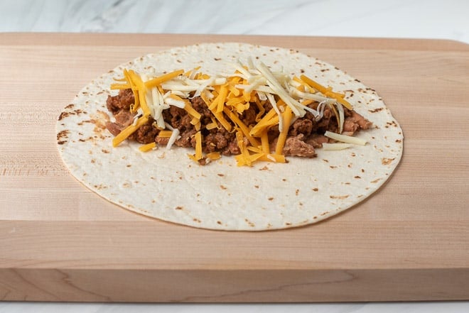 A tortilla topped with a beef and bean mixture and shredded cheese.