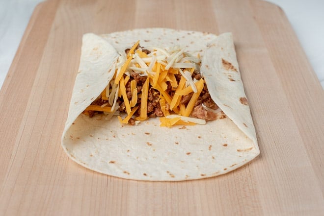 A tortilla filled with beef, beans, and cheese is rolled up.