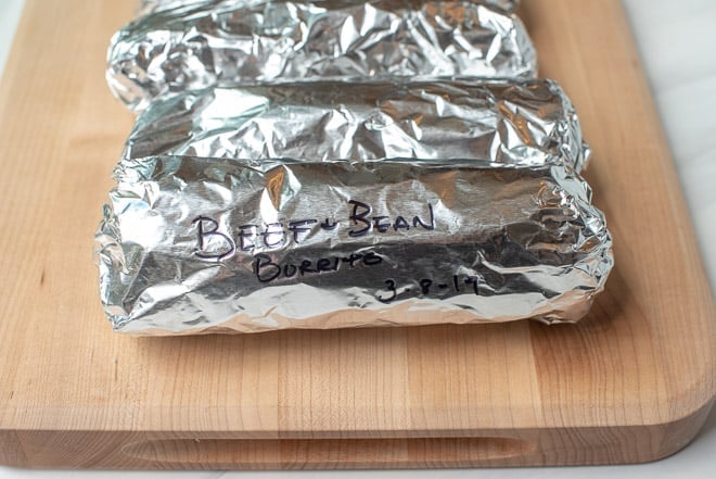 Foil wrapped burritos on a cutting board.