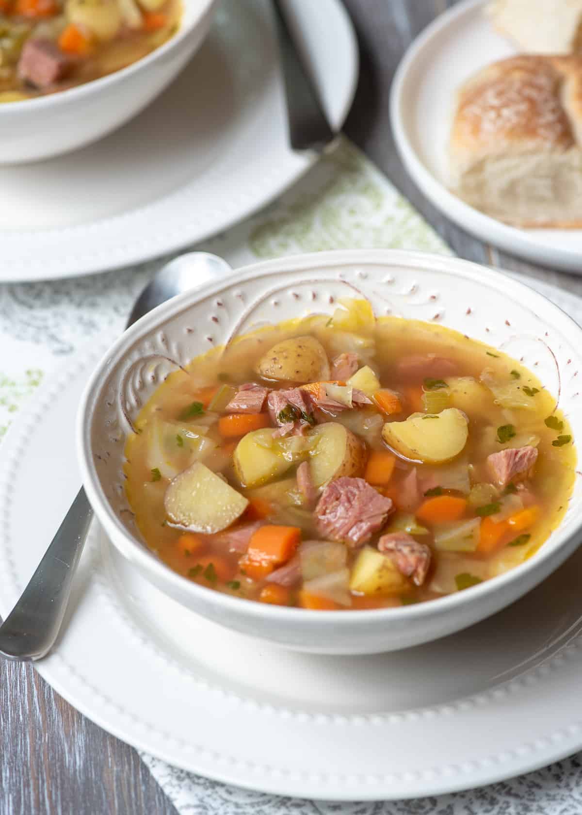 A spoon resting next to a bowl of corned beef and cabbage soup.