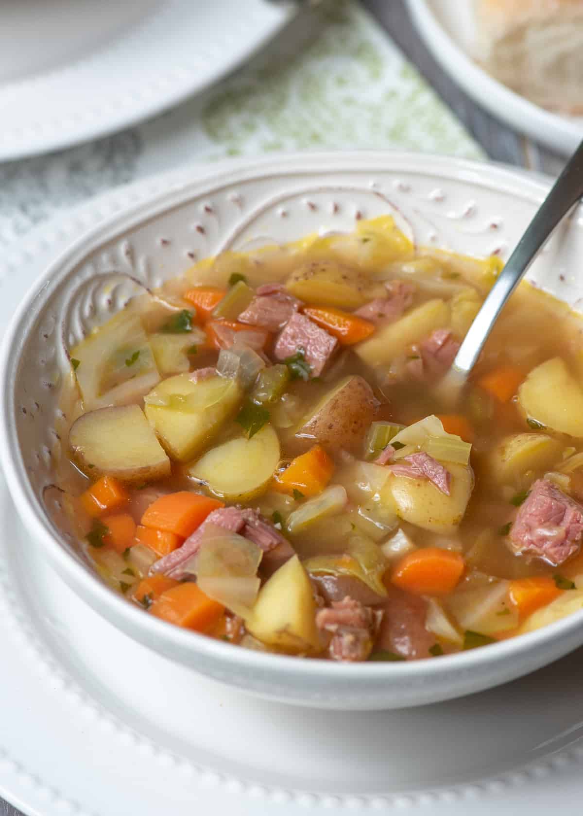 A spoon resting in a bowl of corned beef and cabbage soup.