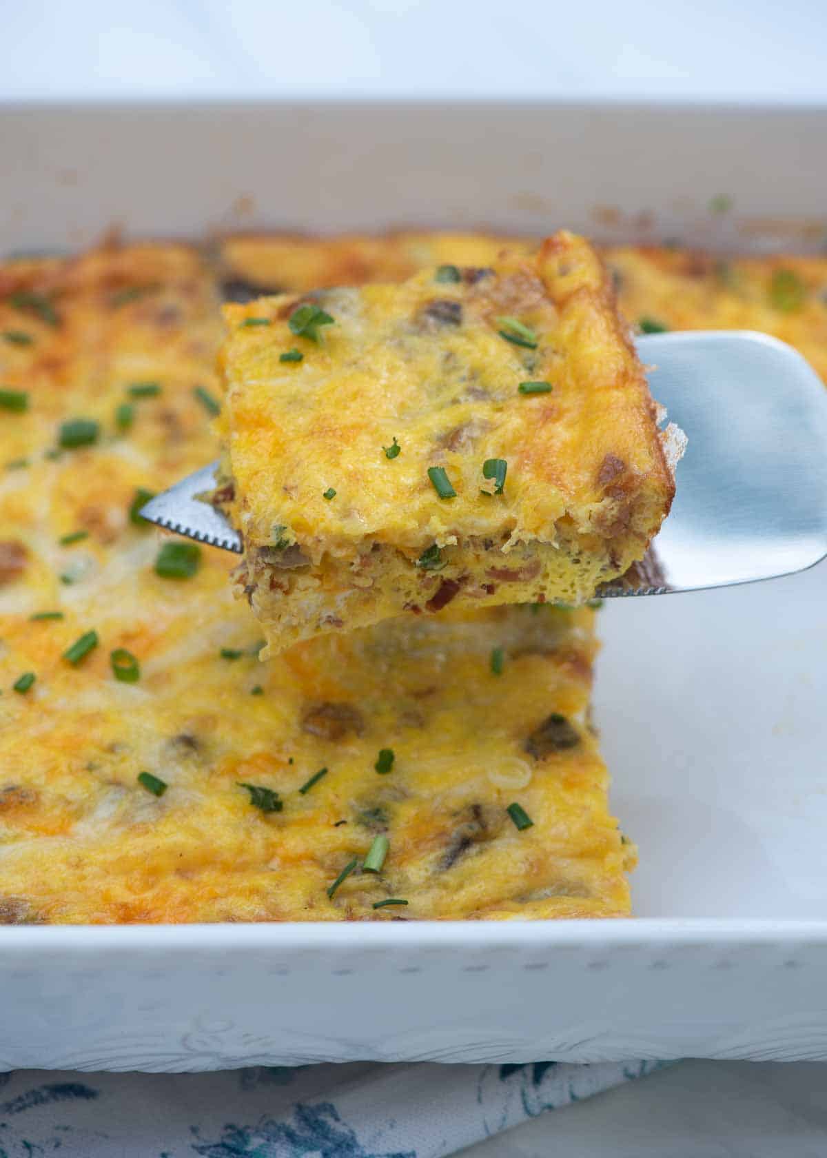 A spatula lifting a slice of crustless quiche from a baking dish.