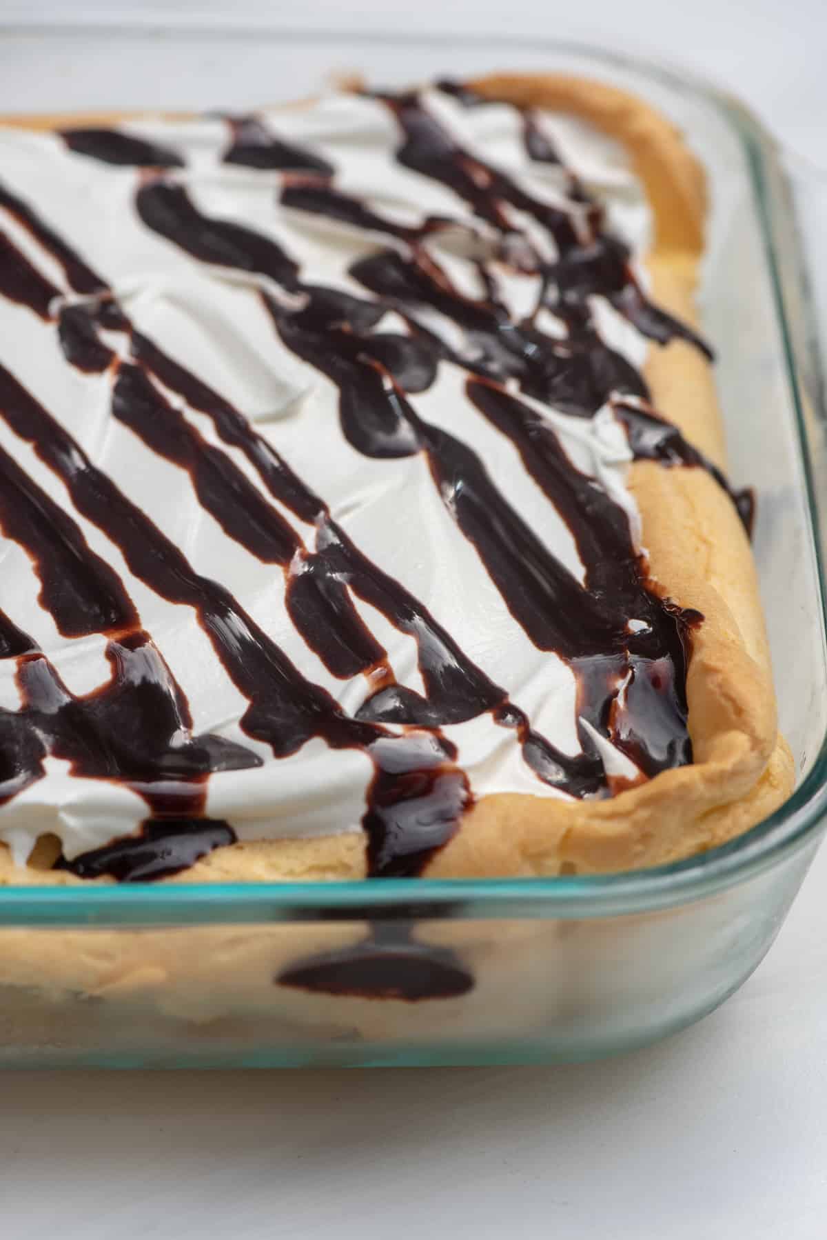 A creamy dessert in a glass baking dish topped with fudge sauce.