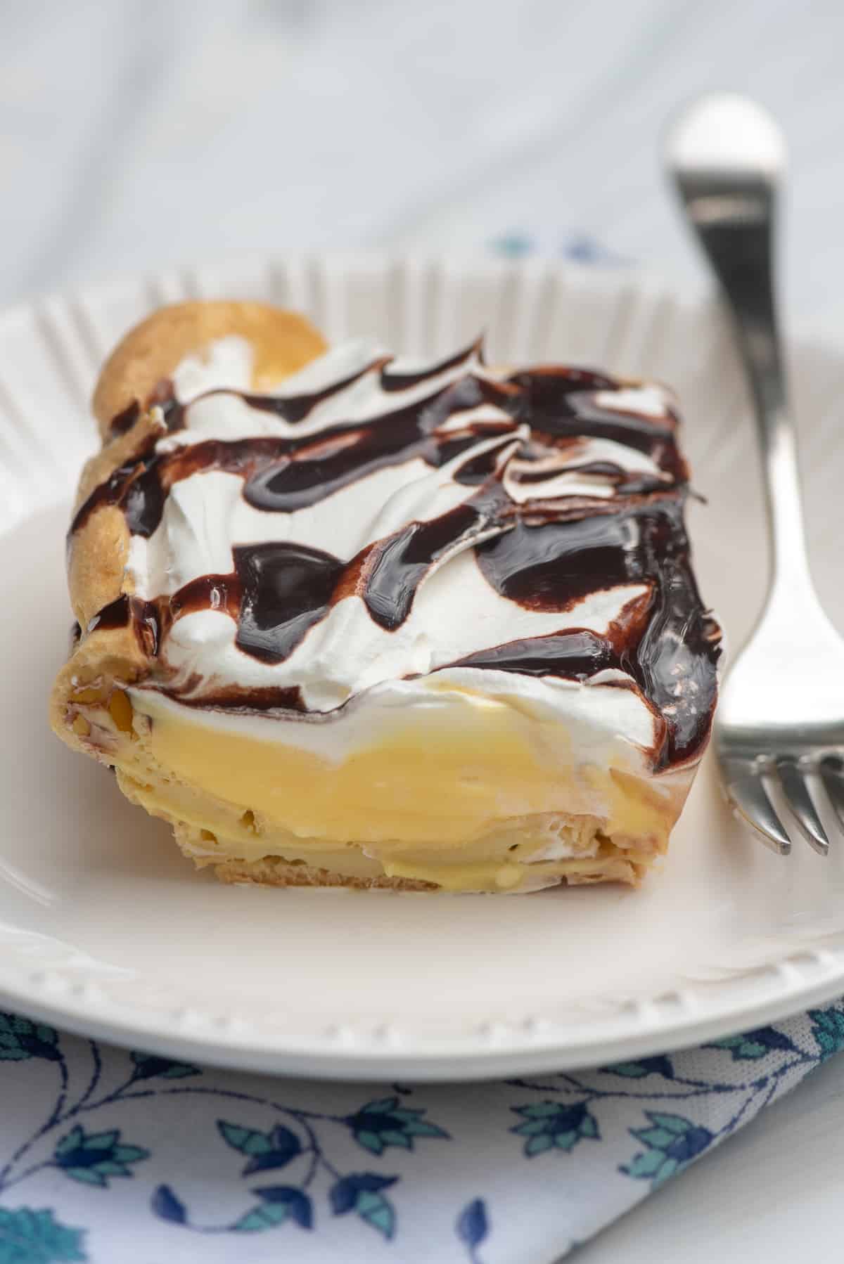 A slice of cream puff dessert on a white plate with a fork.
