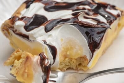 A piece of creamy dessert topped with chocolate with a fork on a white plate.