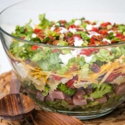 A glass bowl filled layers of bow tie pasta, greens, ham, and vegetables.