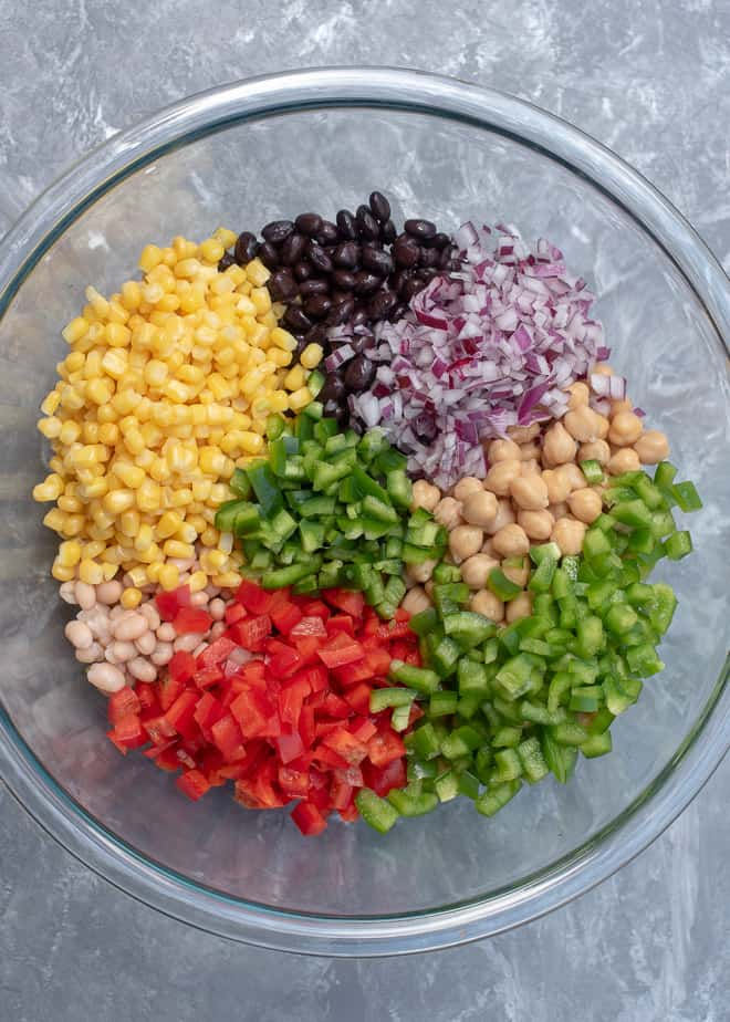 Beans, red onion, peppers, and corn in a large glass mixing bowl.