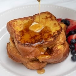 Syrup is poured over two pieces of french toast with butter.