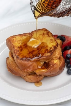 Syrup is poured over two pieces of french toast with butter.