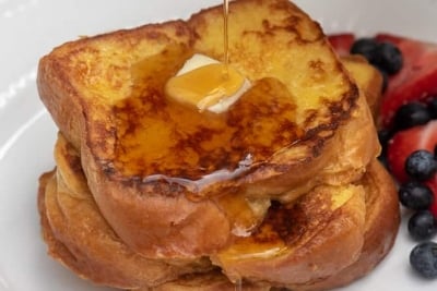 Syrup is poured over two pieces of french toast with butter.