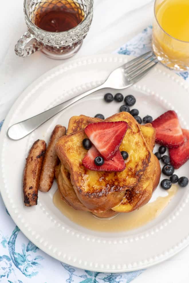French toast with berries and sausage on a white plate.