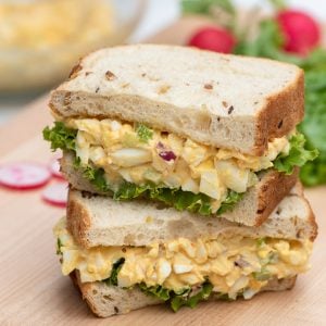 An egg salad sandwich with lettuce cut in half and stacked on a cutting board.
