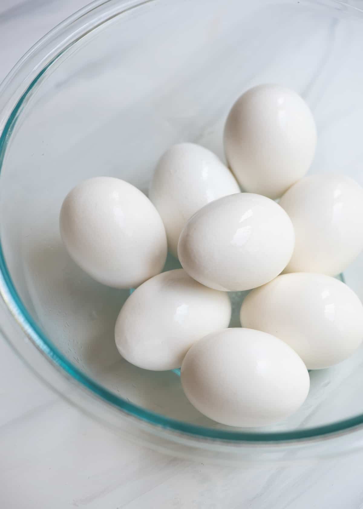 A glass bowl filled with hard boiled eggs.