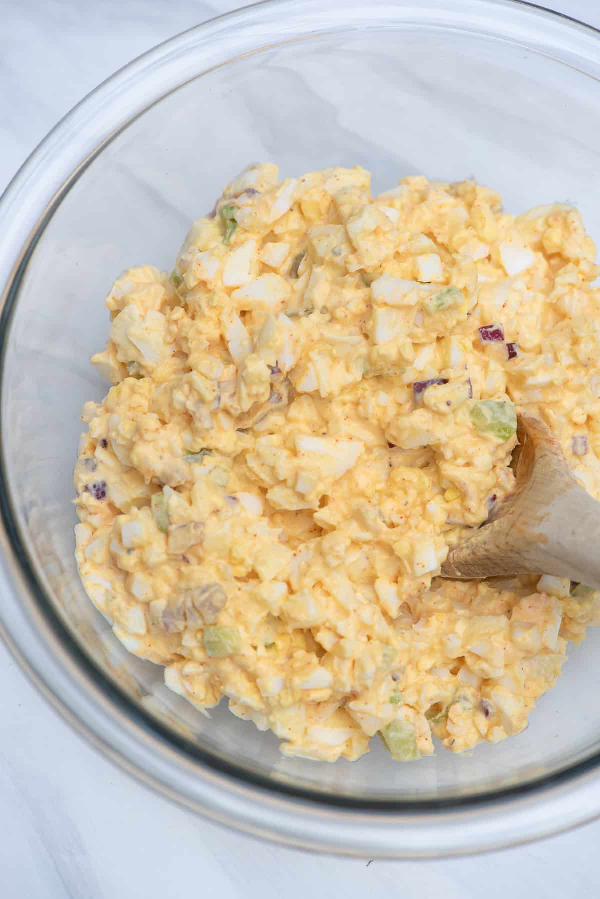 Egg salad in a bowl with a wooden spoon.