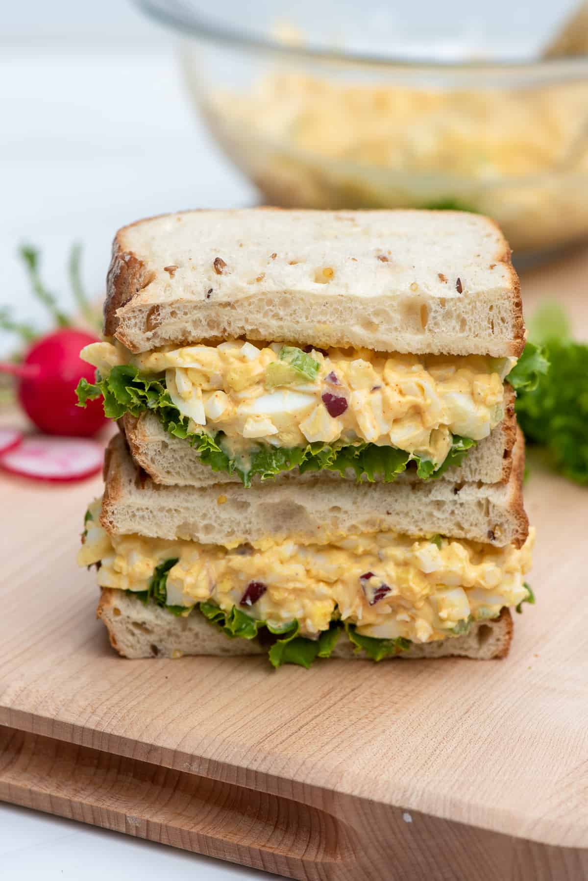 An egg salad sandwich sliced in half and stacked on a cutting board.