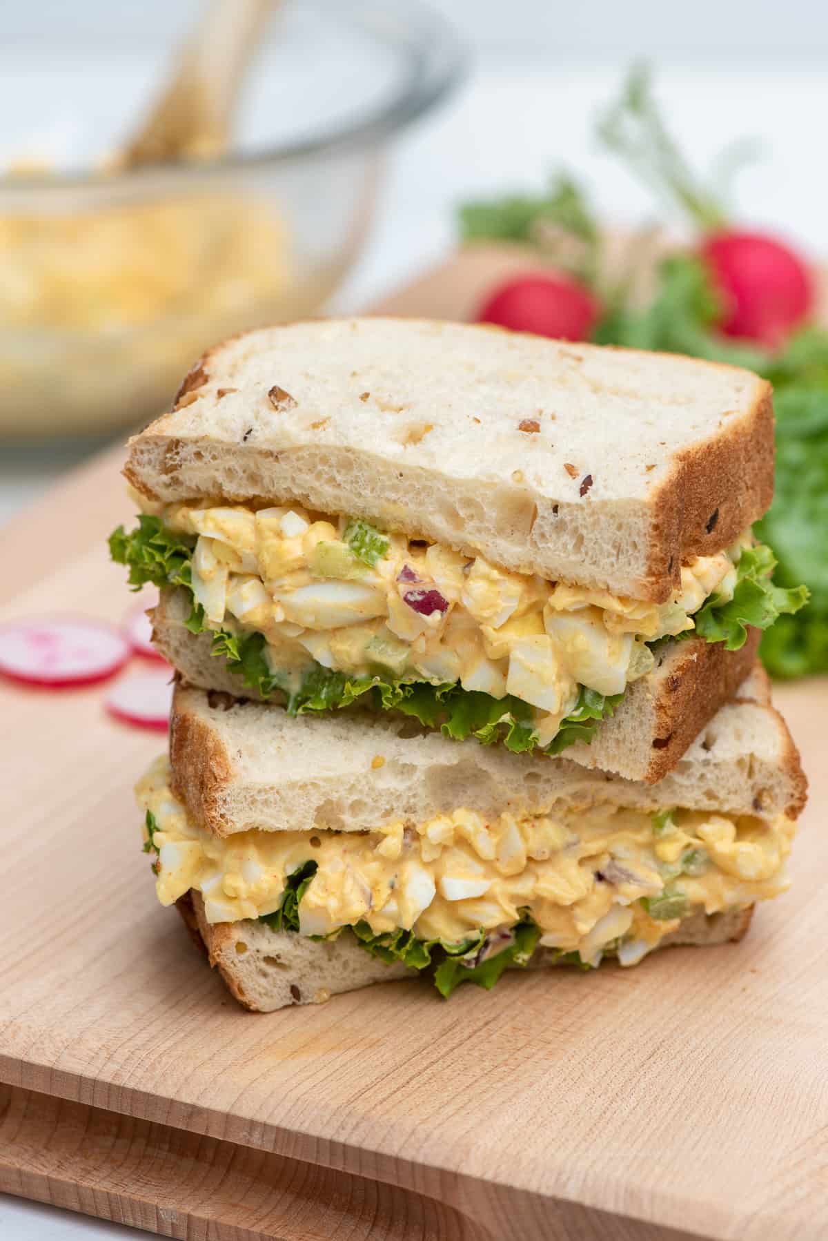 An egg salad sandwich with lettuce cut in half and stacked on a cutting board.