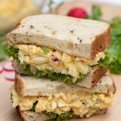 An egg salad sandwich cut in half and stacked on a cutting board.