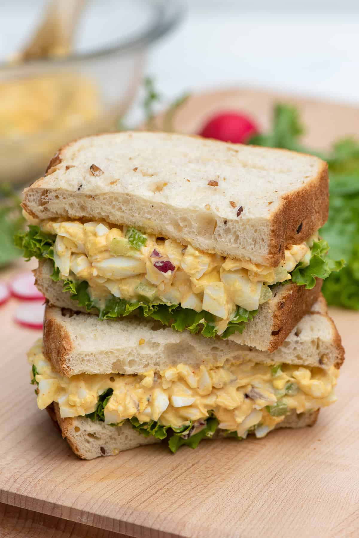 An egg salad sandwich cut in half and stacked on a cutting board.