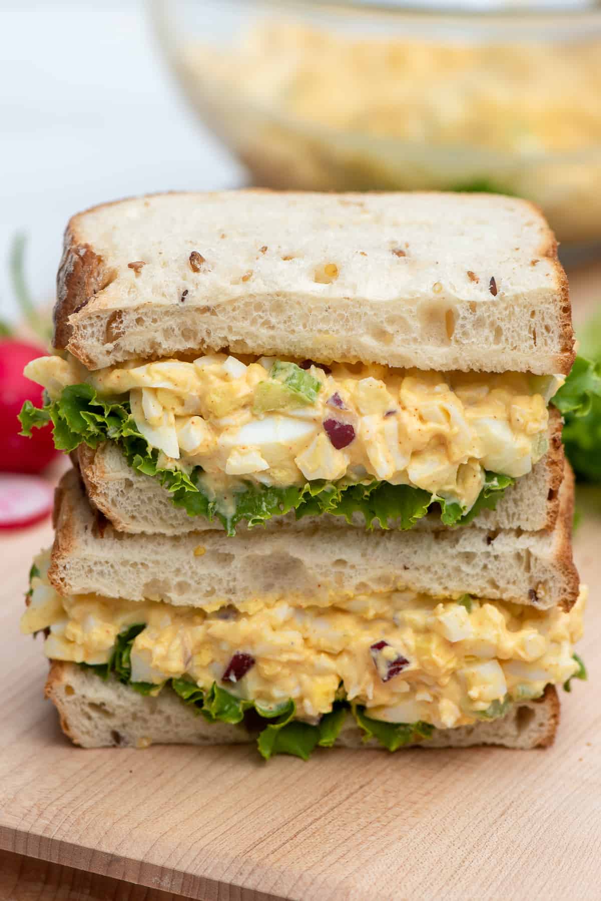 An egg salad sandwich cut in half and stacked on a cutting board.