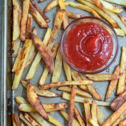 French fries on a baking sheet with a small bowl of ketchup.