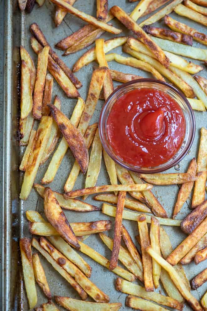 French fries on a baking sheet with a small bowl of ketchup.