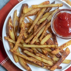 A white plated filled with fries and a small bowl of ketchup.