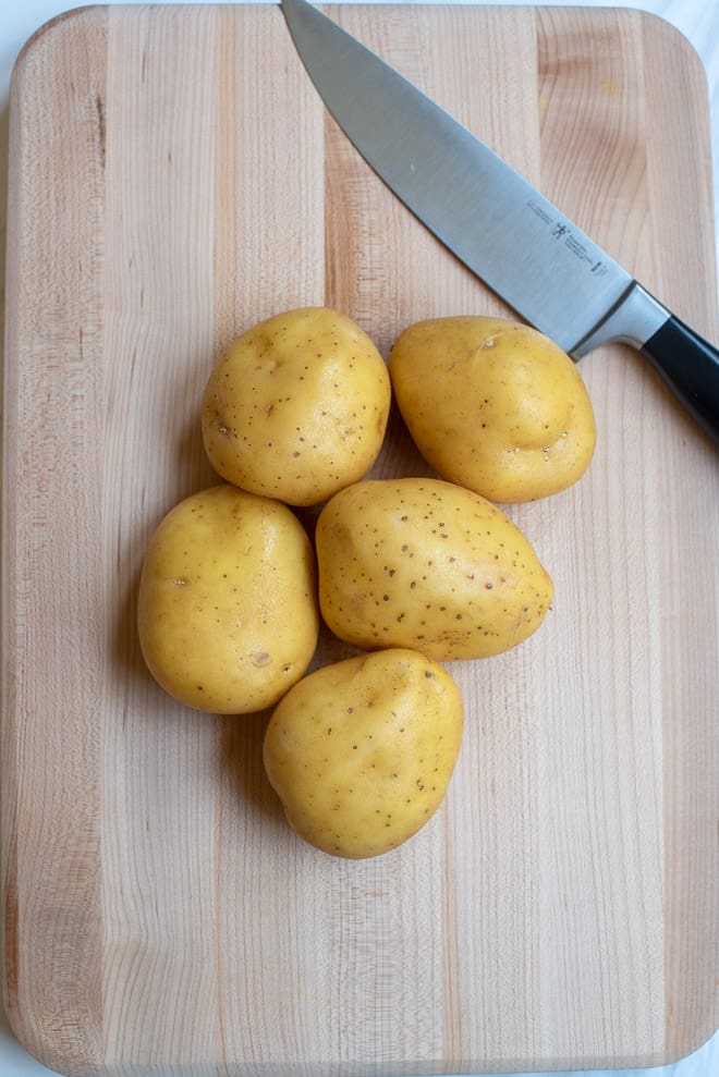 Five Yukon Gold potatoes on a cutting board with a knife.