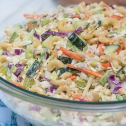 A close up of a bowl of coleslaw with macaroni and slices of cucumber.