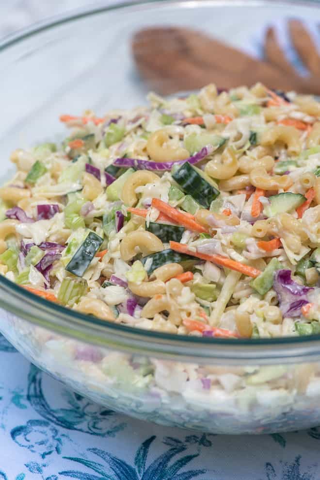 A close up of a bowl of coleslaw with macaroni and slices of cucumber.